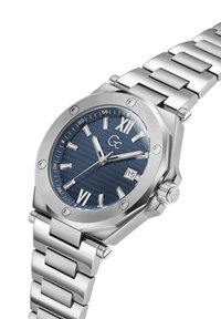 Sudraba nerūsējošā tērauda pulkstenis ar oktagona korpusu, zilu teksturētu ciparnīcu, baltām stundu atzīmēm un datuma displeju. Metāla saite.