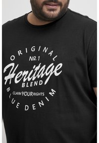Juodas medvilninis marškinėliai su ryškiais baltais užrašais: "Original No.1 Heritage Blend Išsaugokite savo teises Mėlyna džinsinė medžiaga," su apvaliu logotipo dizainu.