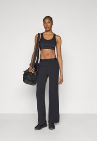 Čierny atletický crop top a široké nohavice z mäkkej látky, doplnené čiernou kabelkou na rameno. Obuv tvoria čierne tenisky.