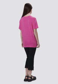 Camiseta rosa de manga corta con un corte relajado, combinada con unos pantalones negros tobilleros con un acabado de dobladillo en forma de escallón. Sandalias negras de suela gruesa.
