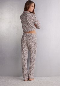 Bloemmotief pyjama set in zachte stof; knoopsluiting shirt met kraag, lange mouwen en bijpassende losse broek. Lichte kleuren domineren.