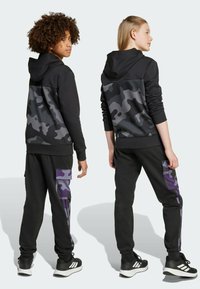 Black hoodie with gray camouflage pattern on the back, paired with black pants featuring purple camo accents and elastic cuffs.
