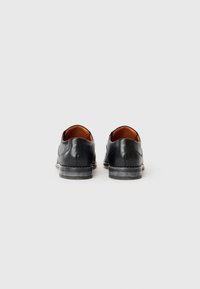 Zapatos de cuero negro con una textura suave y un diseño de punta redondeada. Cuentan con un tacón bajo y apilado, y un forro interior marrón que contrasta.