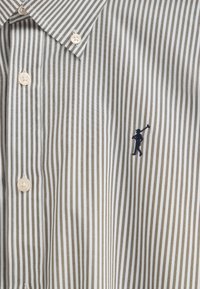 Skjorta med knappar i ljus beige och vita ränder, med en liten mörkblå broderad figur och ljusa knappar. Slät tygstruktur.