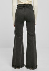 Vaqueros negros de campana con cintura alta, con una textura clásica de denim, leves desgastes y dobladillos doblados en el remate.