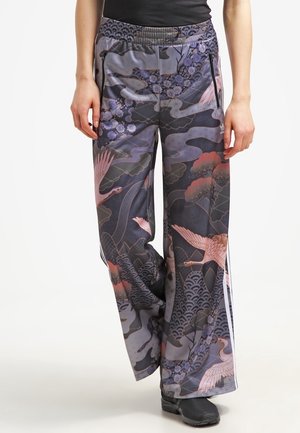 Woman wearing wide-leg pants with a dark floral and bird pattern, side zip pockets, and black shoes.