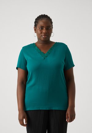 Teal short-sleeve top with a lace-trimmed V-neck. Smooth texture and relaxed fit, paired with black pleated trousers.