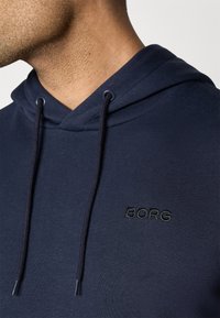 Sweatshirt azul marinho com um tecido texturizado; apresenta um capuz com cordão e o logótipo "BORG" bordado em preto no peito.