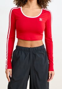 Röd kortärmad långärmad topp med vita accenter och rund halsringning. Har en figurnära silhuett och två vita ränder längs ärmarna.