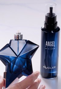 Sternförmige blaue Glasparfümflasche mit metallischen silbernen Akzenten, neben einer dunkelblauen Sprühflasche mit der Aufschrift "ANGEL" von Mugler.