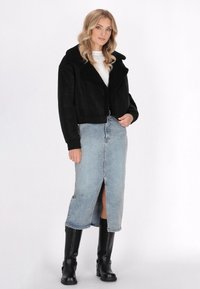 Schwarze, verkürzte Jacke mit einem Kragen aus Kunstfell, kombiniert mit einem hellblauen Denim-Rock mit Schlitz vorne und schwarzen kniehohen Stiefeln.