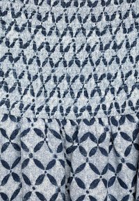 Il tessuto blu con motivo presenta una parte superiore arricciata e una parte inferiore plissettata, mostrando un design floreale con tonalità scure e chiare alternate.