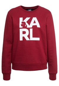 Röd sweatshirt med rund halsringning, med en stor vit "KARL"-logotyp och en silhuett-design, tillverkad av mjukt bomullsmaterial.