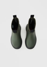 Stivali alla caviglia in gomma verde con finitura liscia, suola nera e piccolo anello sul retro per una facile vestibilità.