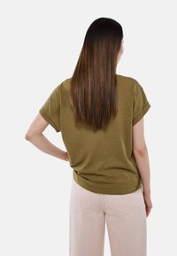 Chemise vert olive à manches courtes avec poignets retroussés, texture douce, coupe ample, associée à un pantalon large rose clair.