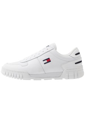 Biały niskoprofilowy sneaker z żłobioną podeszwą i prostokątnym logo w kolorach czerwonym, białym i niebieskim po boku i na pięcie, bez widocznie zawiązanych sznurówek.