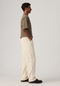 Μπλούζα από βαμβακερό μείγμα σε ελιά πράσινο με κοντά μανίκια, συνδυασμένη με μπεζ cargo παντελόνι με λεπτές ρίγες, πλαϊνές τσέπες και λεπτομέρεια λογότυπου.