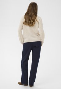 Beige pulóver, sötétkék farmernadrág és barna lábbeli. A pulóver hosszú ujjú, míg a nadrág egyenes szabású, klasszikus dizájnnal.