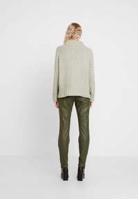 Grön stickad tröja med hög krage och ribbad nederdel, tillsammans med olivgröna läderbyxor. Texturen är mjuk och fyllig.