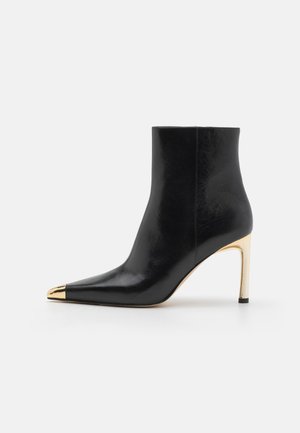Black leather ankle boot with a pointed toe, gold metallic cap, and a slender high heel. Smooth texture with a minimal design.