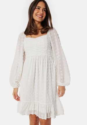 Witte jurk van gestructureerde stof met pofmouwen, gerimpelde taille en gelaagde ruffle zoom. Bevat geborduurde bloemenaccenten.