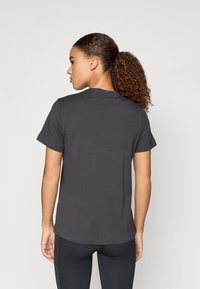 Szürke, rövid ujjú póló, kerek nyakkal. Pamut anyag, laza szabás, egyenes alj, fekete leggings-szel viselve.