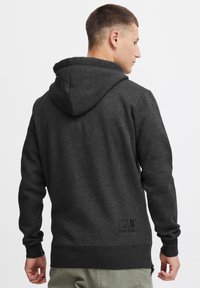 Sudadera gris oscuro con capucha ajustable, puños y dobladillo acanalados. Presenta un detalle de logo texturizado cerca de la parte inferior posterior. Tejido suave.