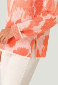 Stickad tröja i orange och vit melerad design, med långa ärmar, ribbade muddar och sidokilar. Mjuk, strukturerad yta.