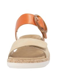 Sandale en nubuck beige et cuir orange avec une boucle décorative ronde, une semelle texturée couleur tan, et une sangle réglable.