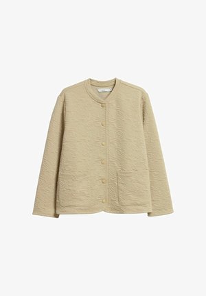 Beige tikattu takki, jossa on pyöreä kaula-aukko, painonapit, kaksi etutaskua ja koko kankaan kattava teksturoitu kiertokuvio.