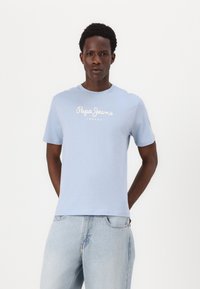 Ανοιχτό μπλε βαμβακερό T-shirt με κοντά μανίκια. Διαθέτει το λογότυπο "Pepe Jeans London" τυπωμένο σε λευκό πάνω από το στήθος. Χαλαρή εφαρμογή.
