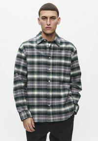 Green and gray plaid shirt made of flannel fabric; features a button-up front and a collar, with long sleeves and a loose fit.