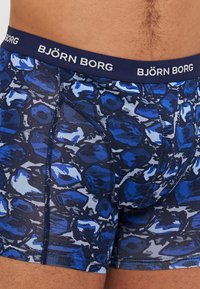 Plave bokserice s uzorkom s tamnoplavim pojasom s "BJÖRN BORG" brandingom, izrađene od elastičnog materijala s glatkom teksturom.