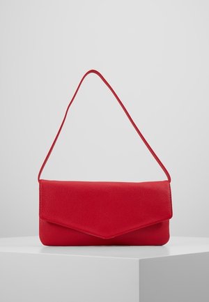 Czerwona, fakturowana skórzana torba na ramię w stylu kopertówki z cienkim paskiem, wyeksponowana na białym piedestale na tle szarej ściany.