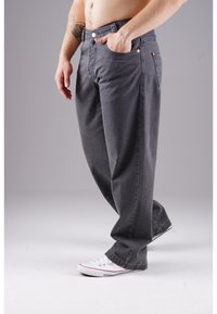 Gray men's jeans with a relaxed fit, visible stitching, and buttoned pockets; paired with white sneakers.