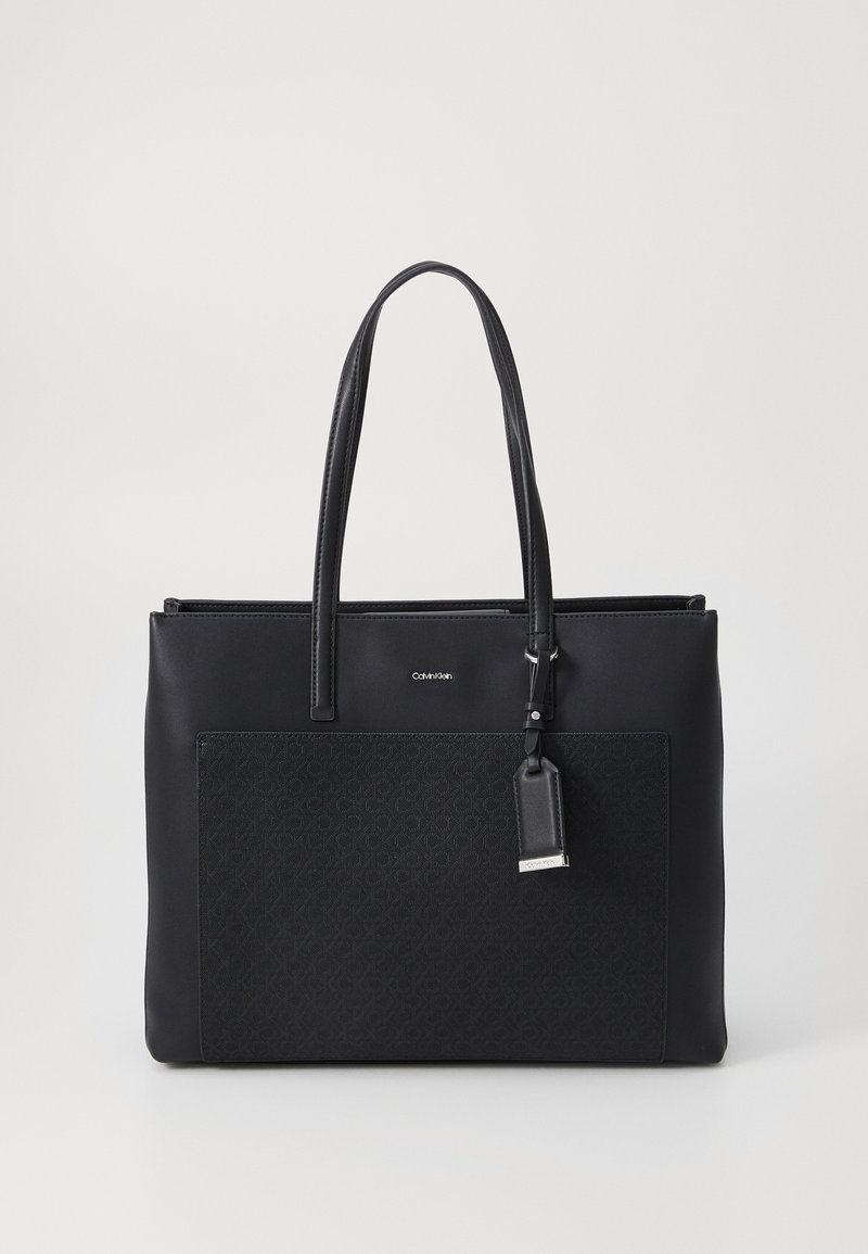 Svart lær tote bag med en teksturert frontpanel, glatte håndtak og en avtagbar merkelapp. Har et minimalistisk design og glidelåsåpning.