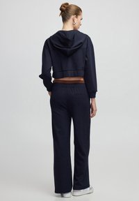 Sudadera navy corta con capucha ajustable y dobladillo acanalado, combinada con pantalones de pierna ancha de talle alto que cuentan con una cinturilla elástica.