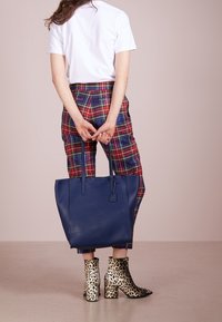 Sininen nahkainen olkalaukku, jossa on kaksi kahvaa, sileä pinta ja suorakaiteen muotoinen. Yhdistetty ruudullisiin housuihin ja leopardikuvioisiin saappaisiin.