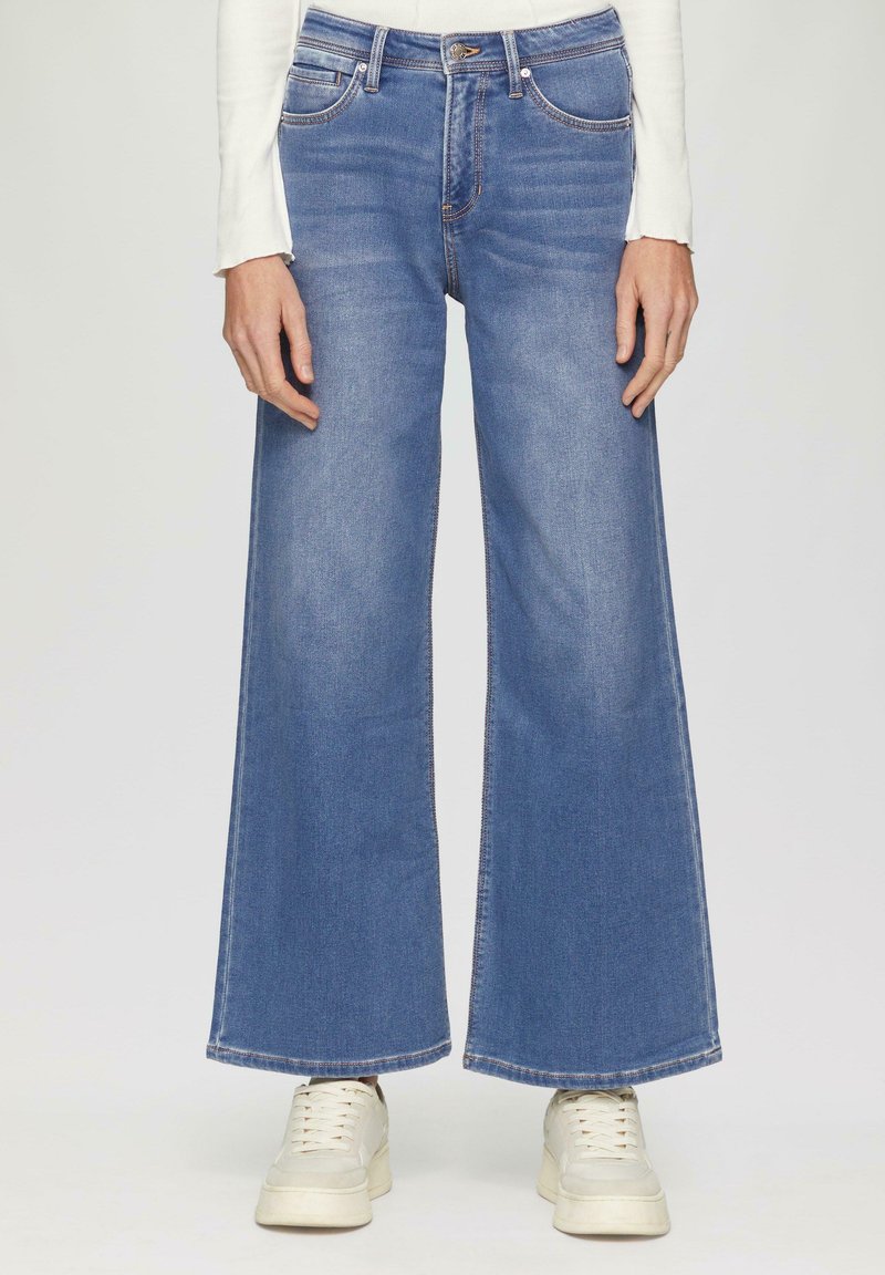 Wijdvallende blauwe denim jeans van katoen. Heeft een hoge taille, vijf zakken en contrasterende stiksels. Gecombineerd met witte sneakers.