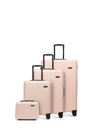 Quatre valises rigides beiges avec poignées et roues noires, disposées par taille du plus petit au plus grand sur un fond blanc.