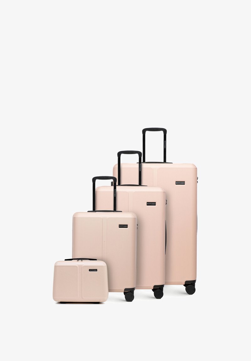 Quatre valises rigides beiges avec poignées et roues noires, disposées par taille du plus petit au plus grand sur un fond blanc.