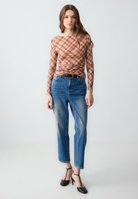 Langarmshirt met een bruin ruitpatroon, gecombineerd met hoge blauwe spijkerbroeken. De outfit heeft een riem en donkere hakken.