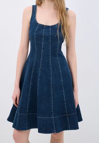 Tummansinisestä denimmekosta, jossa on tiukka yläosa ja leveä helma, näkyvät saumaerot ja leveät olkaimet.