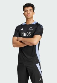 Černý atletický dres se světle modrými akcenty, s nápisem "INEOS" v stříbrné a logem "ALL BLACKS". Vyrobeno z prodyšného materiálu.