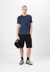 Tricou bleu marin cu mânecă scurtă, cu un finisaj texturat, asortat cu pantaloni scurți cargo negri. O geantă neagră și adidași argintii completează ținuta.