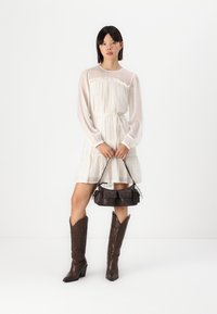 White dress with ruffled neckline and cuffs, short skirt, worn with brown leather cowboy boots and a small dark brown handbag.