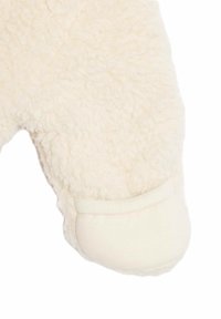 Indumento in pile color crema con una superficie tessuta e pelosa. Presenta un polsino liscio ed elastico alla caviglia per una vestibilità sicura.