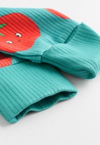 Rippiger türkisfarbener Pullover mit rotem Tomatenmotiv. Weicher Stoff, lange Ärmel und abgerundete Bündchen. Auffälliges süßes Gesichtdetail auf der Tomate.
