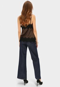 Brązowa satynowa bluzka z czarną koronką w zdobieniu, zestawiona z ciemnoniebieskimi dżinsami o szerokich nogawkach, o gładkiej fakturze i delikatnym połysku. Czarne szpilki.