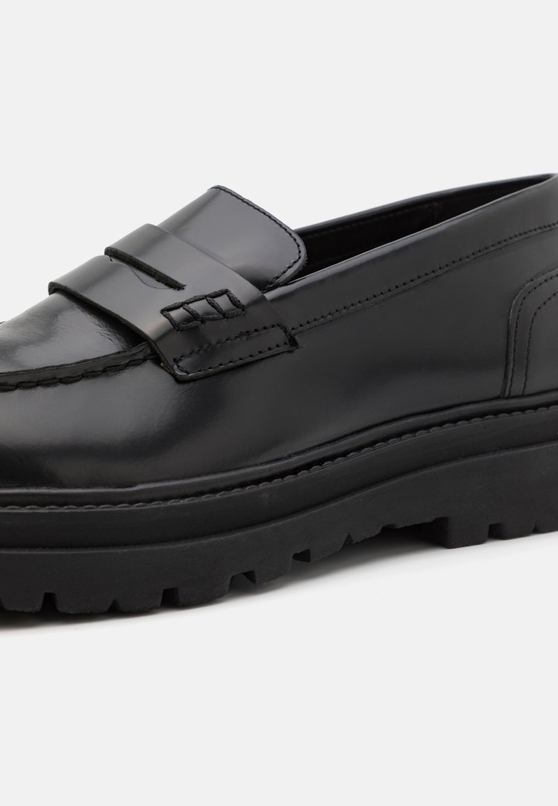 Mocassins en cuir noir avec une finition lisse, dotés d'une sangle décorative, de détails cousus et d'une semelle en caoutchouc épaisse avec des crampons.